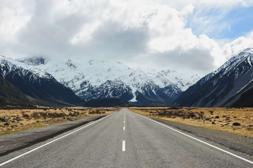 gray concrete road near mountain under white clouds during daytime